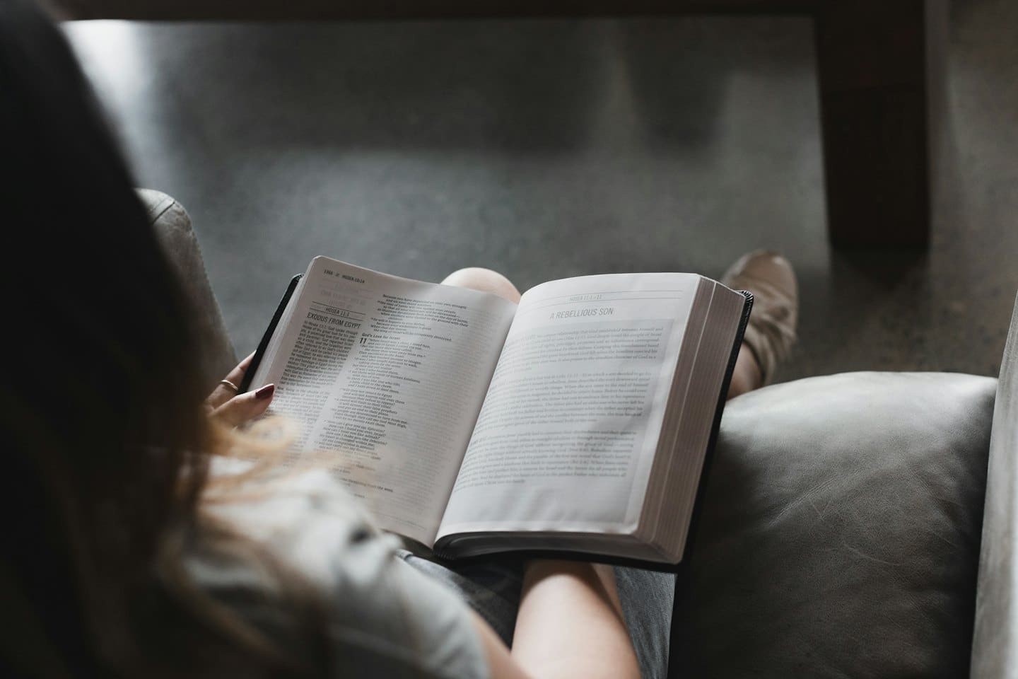 Donna con unghie rosse che legge un libro aperto su una poltrona.