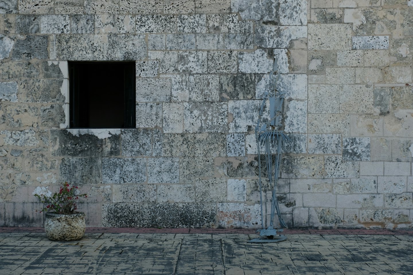 Scultura in metallo accanto a un muro di pietra e una fioriera.